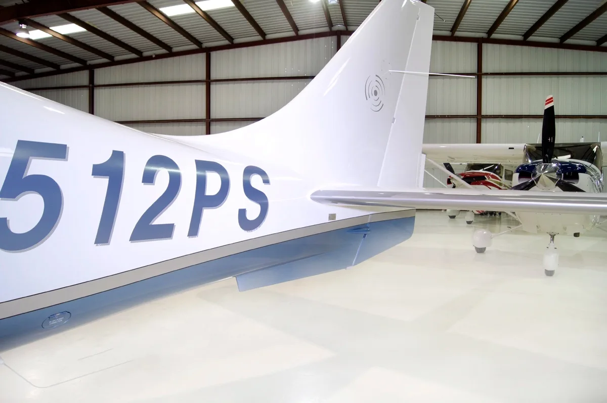A close-up view of the white tail section of the N512PS aircraft, showing the registration number and horizontal stabilizer in a hangar.