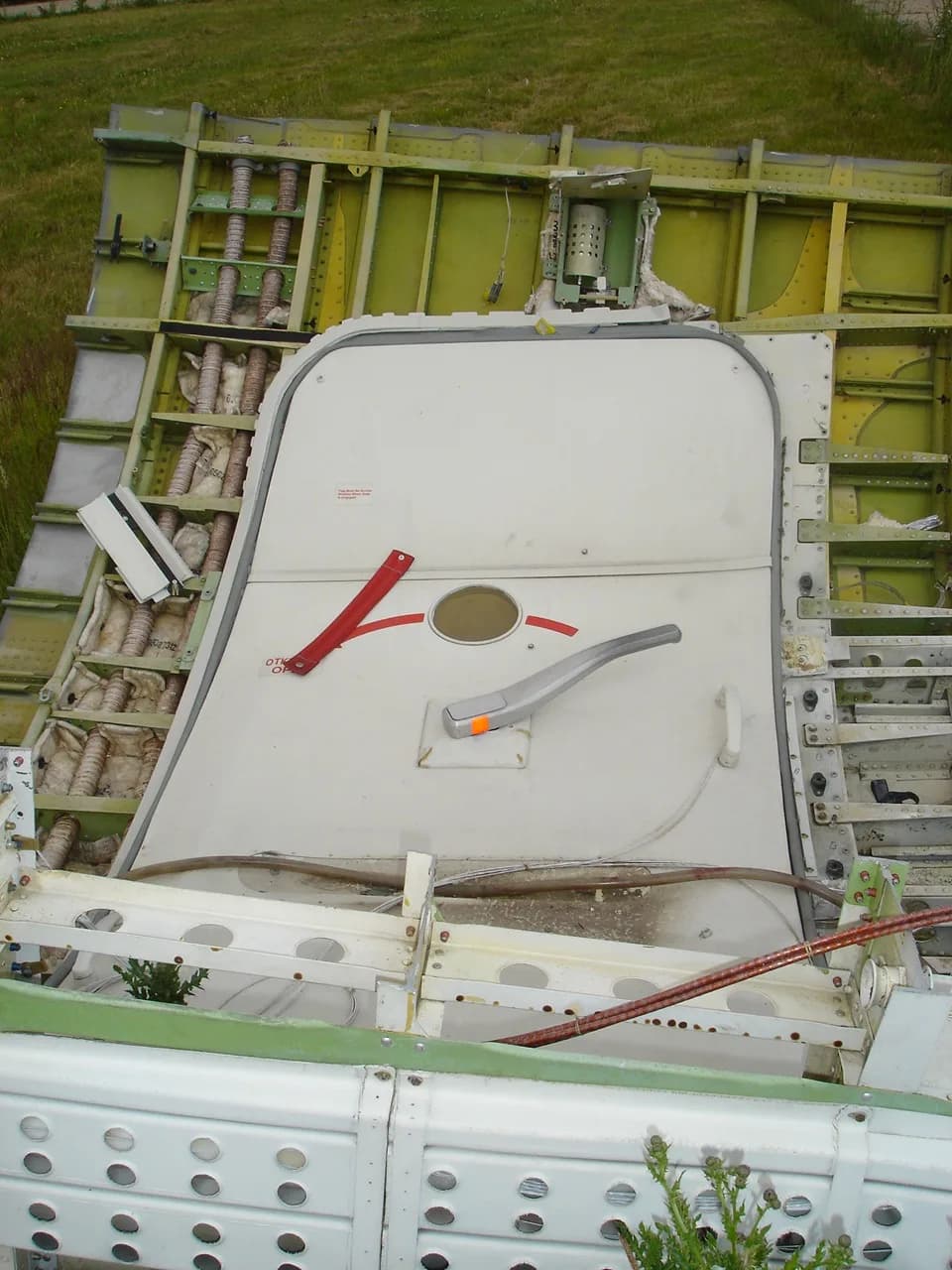 A close-up view of a disassembled aircraft fuselage section with an emergency exit door and exposed internal structure.