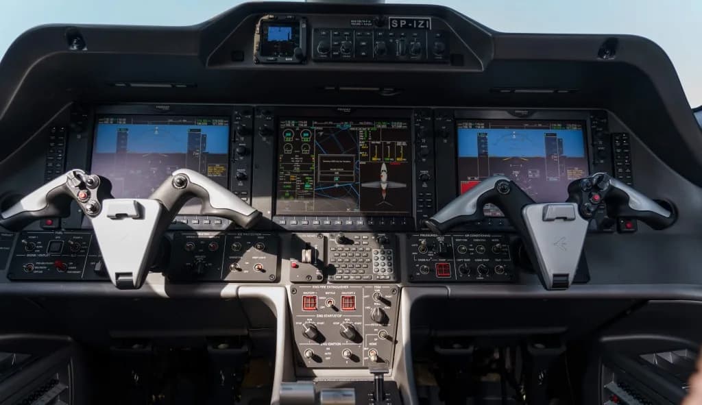 A wide view of a modern aircraft cockpit with multiple large digital displays and dual yokes.
