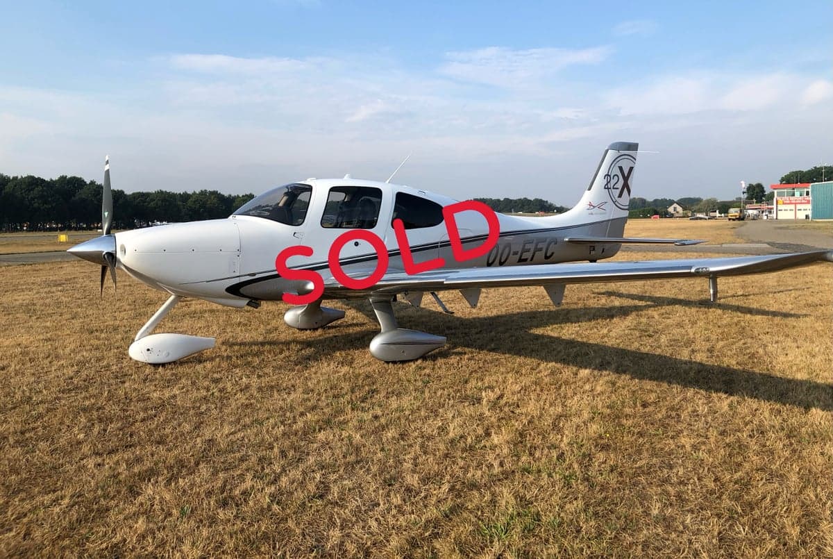A Cirrus SR22T aircraft with registration OO-EFC is parked on a grassy field.