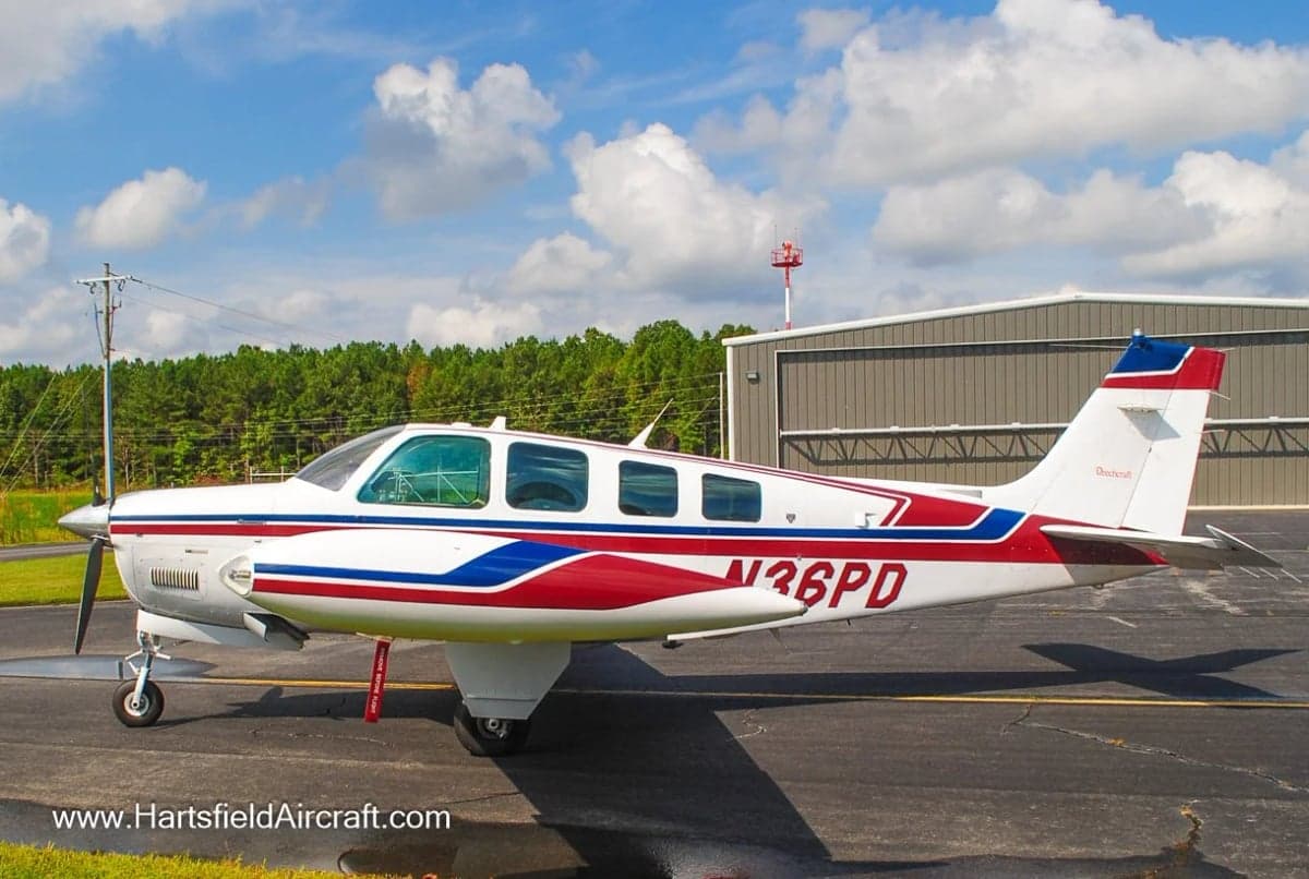 Side view of a Beechcraft Bonanza aircraft with red and blue stripes on the fuselage.