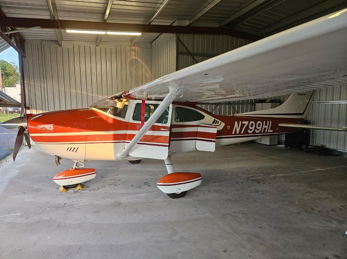 An orange and white Cessna Skylane with registration N799HL is parked inside a hangar.