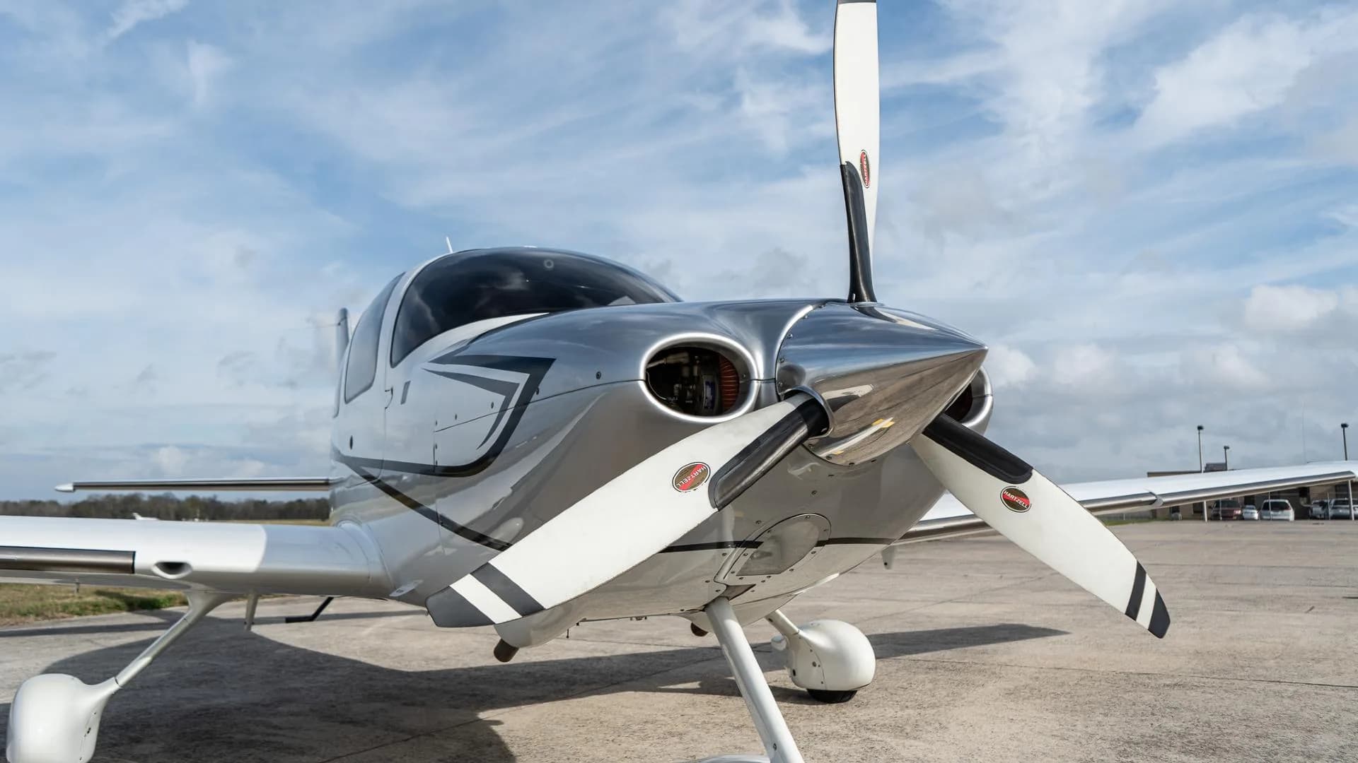Front view of a white Cirrus SR22 aircraft with a three-bladed propeller on an airfield.