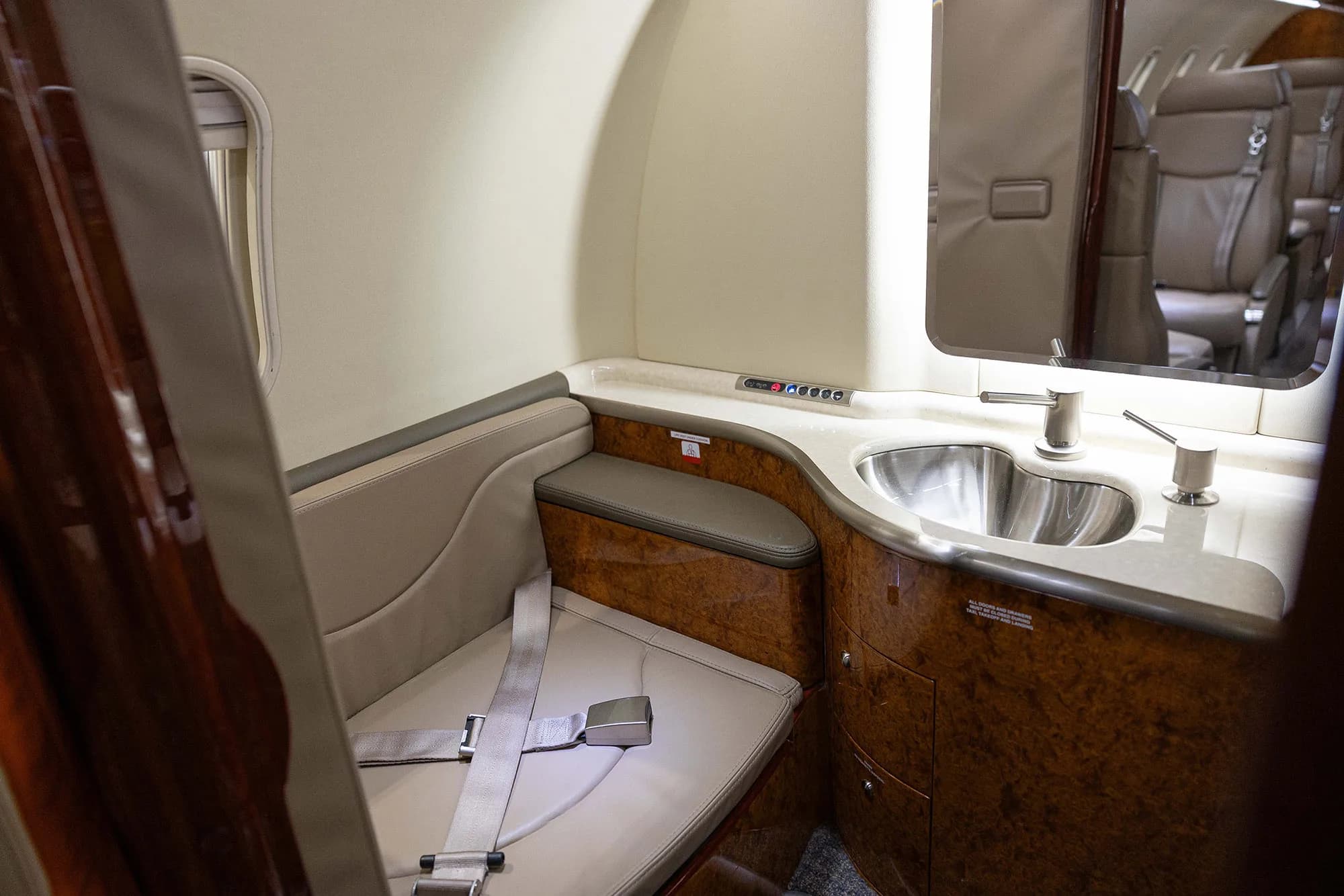 A view of the private jet's lavatory or galley area, featuring a small sink, mirror, and a cushioned seat.