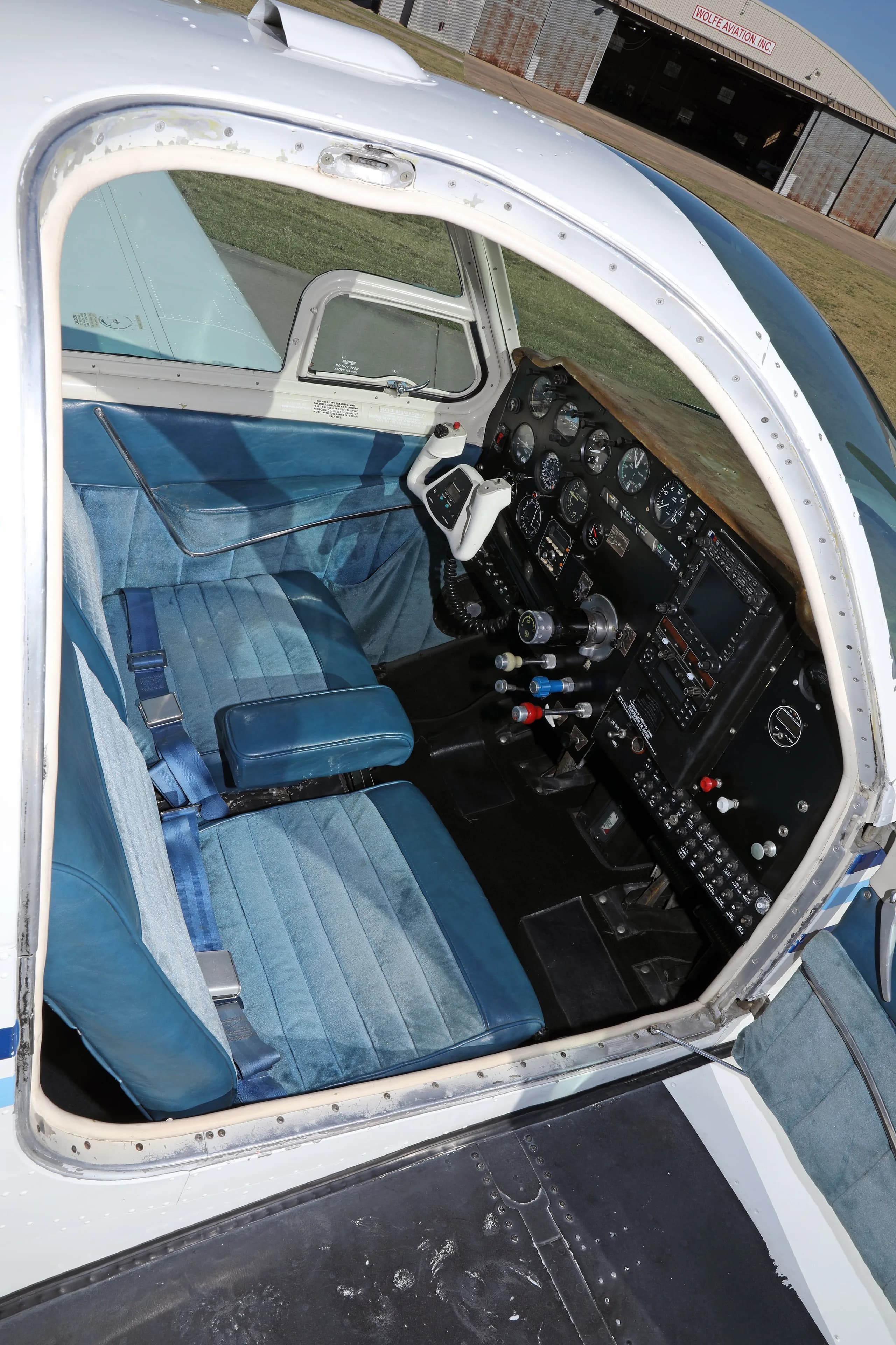 An overhead view into the cockpit of a white aircraft with blue seats and instrument panel, seen through an open door.