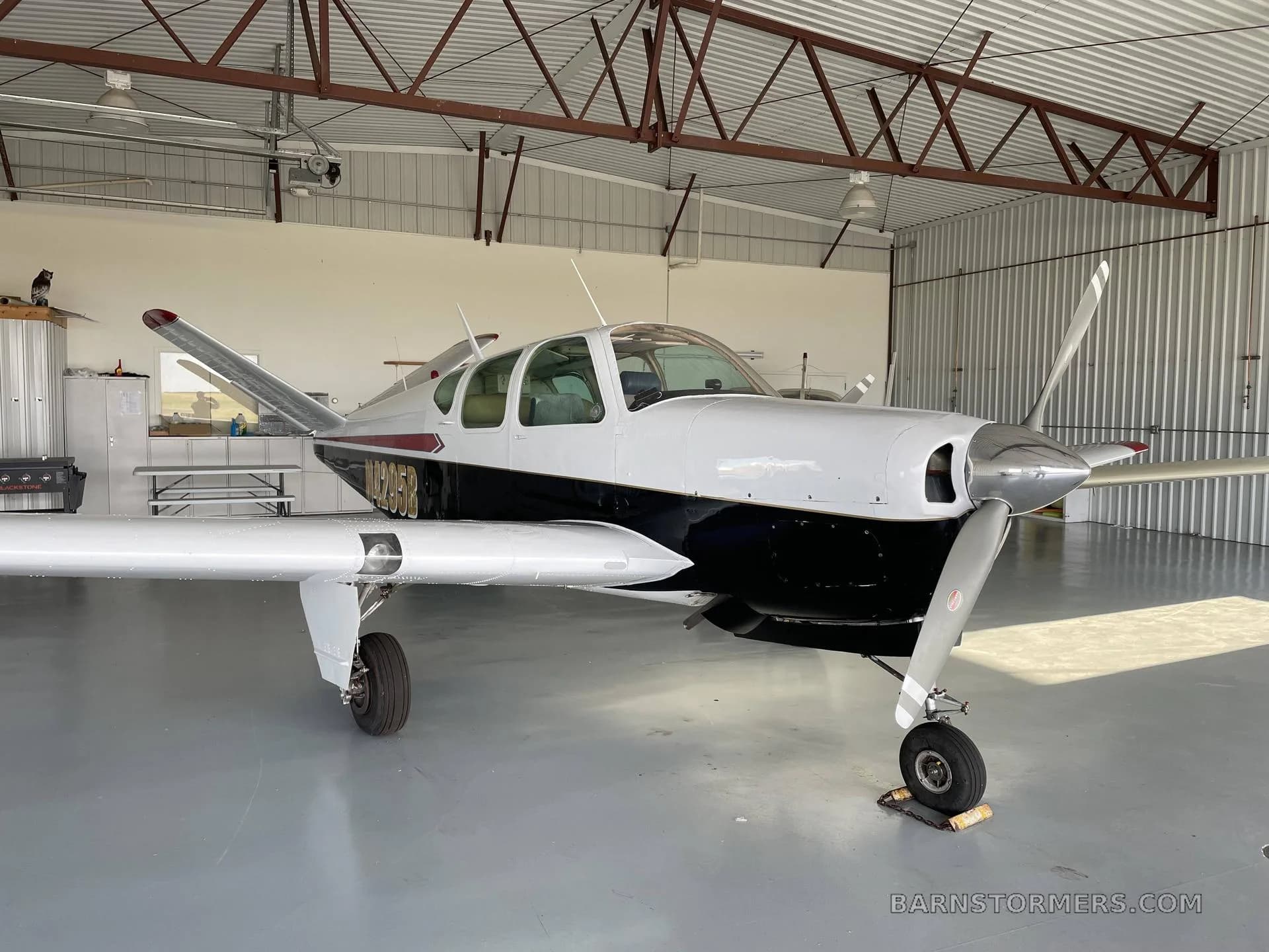 A full front-side view of a white and black single-engine aircraft with registration N14295B parked in a hangar.