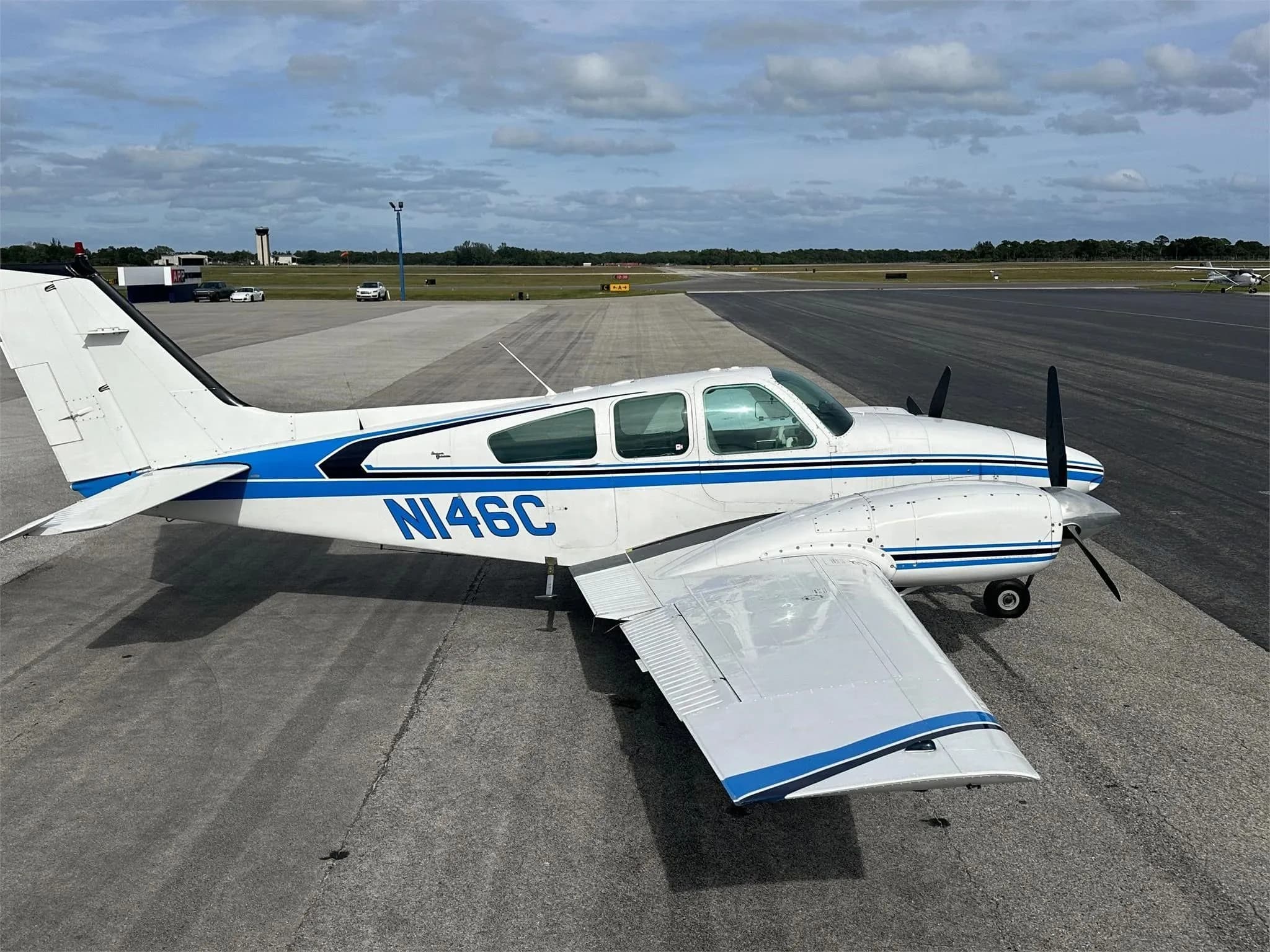 A white and blue twin-engine aircraft, N146C, parked on an airport tarmac with a distant control tower.