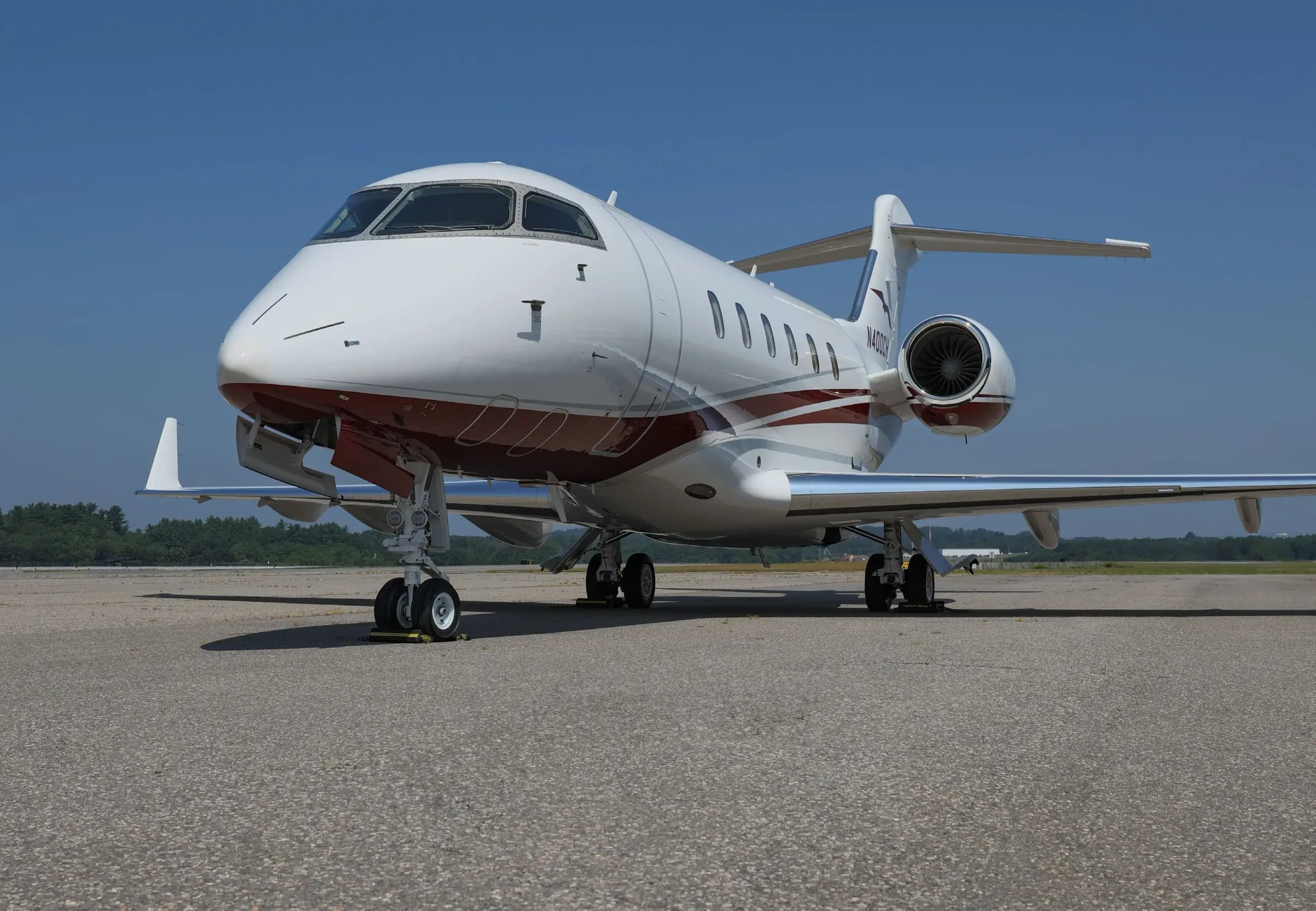 Front-quarter view of a white business jet with red and grey stripes, registration N111EL, parked on an airfield.