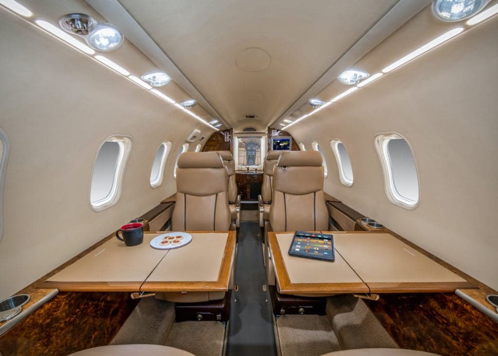 Interior view of the aircraft cabin with tan leather seats and a table with a tablet and mug.