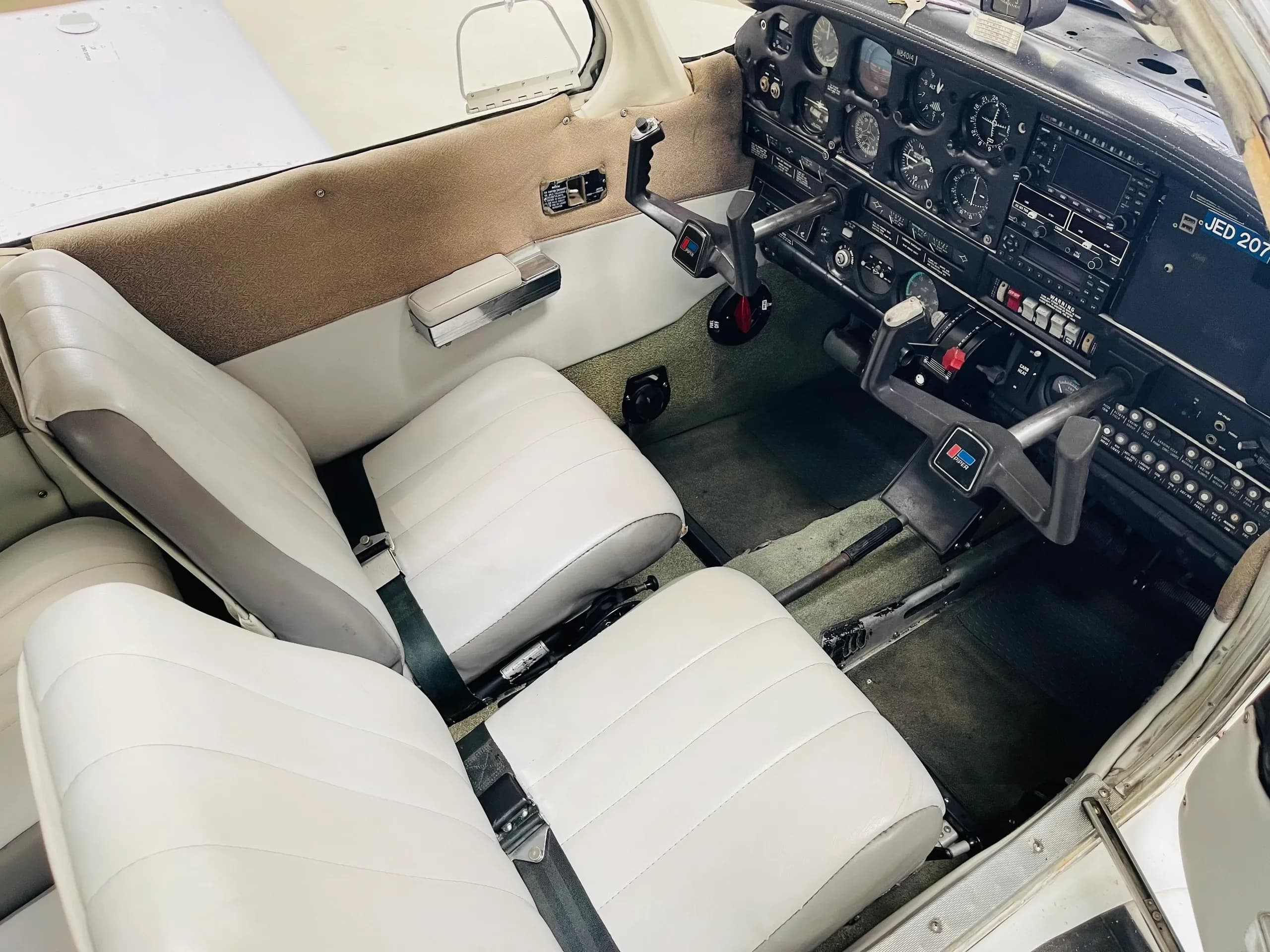 The cockpit interior of a small aircraft, showing the instrument panel, dual yokes, and white front seats.