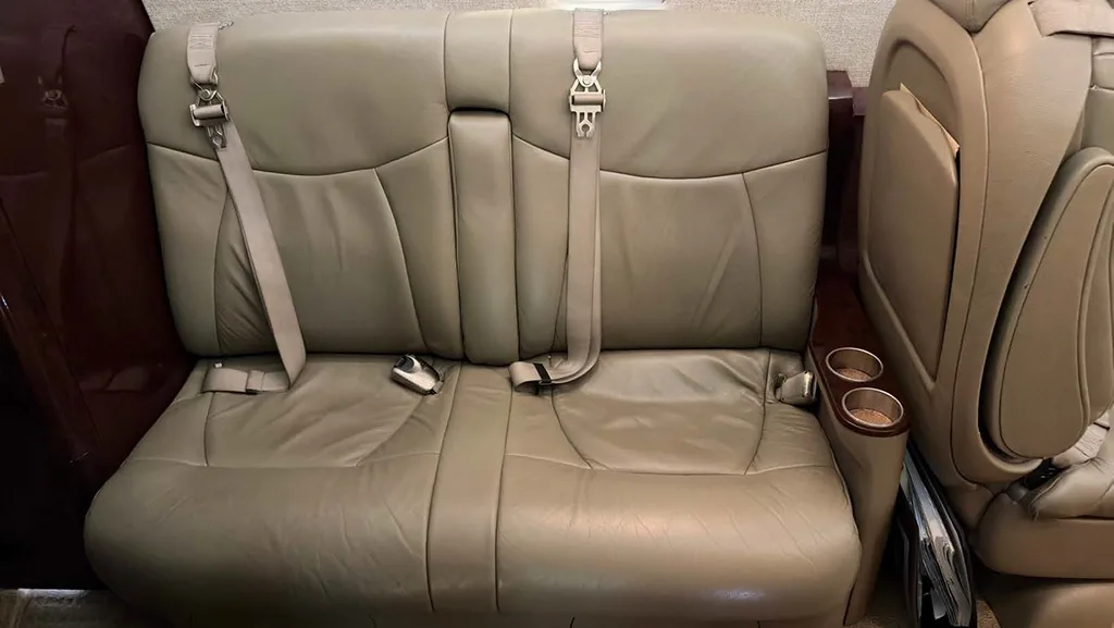 Close-up of a beige leather two-person bench seat with seatbelts and cup holders in the aircraft cabin.