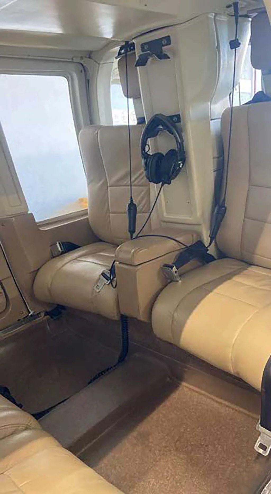 The tan leather passenger seats in the cabin of a helicopter, with a headset hanging.