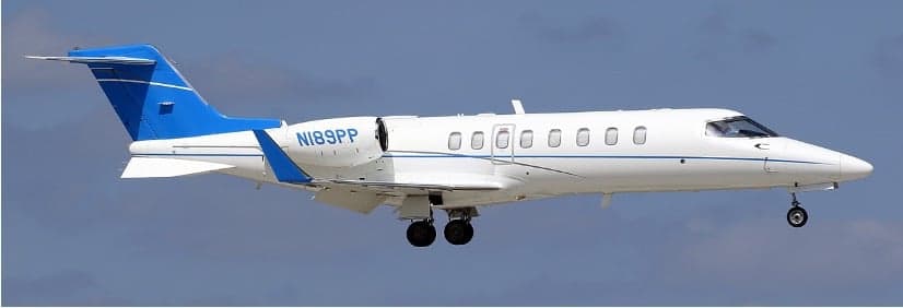 A white and blue Learjet with tail number N189PP is shown in flight.