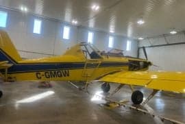 Yellow and blue agricultural aircraft with registration C-GMQW parked inside a hangar.