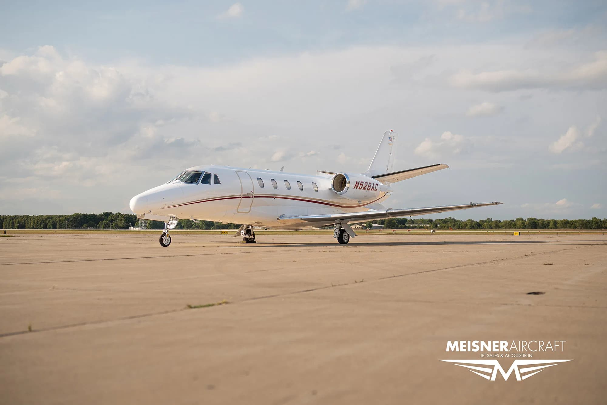 A white business jet with red stripes and registration N528AC parked on an airfield, with a 'Meisner Aircraft' logo.