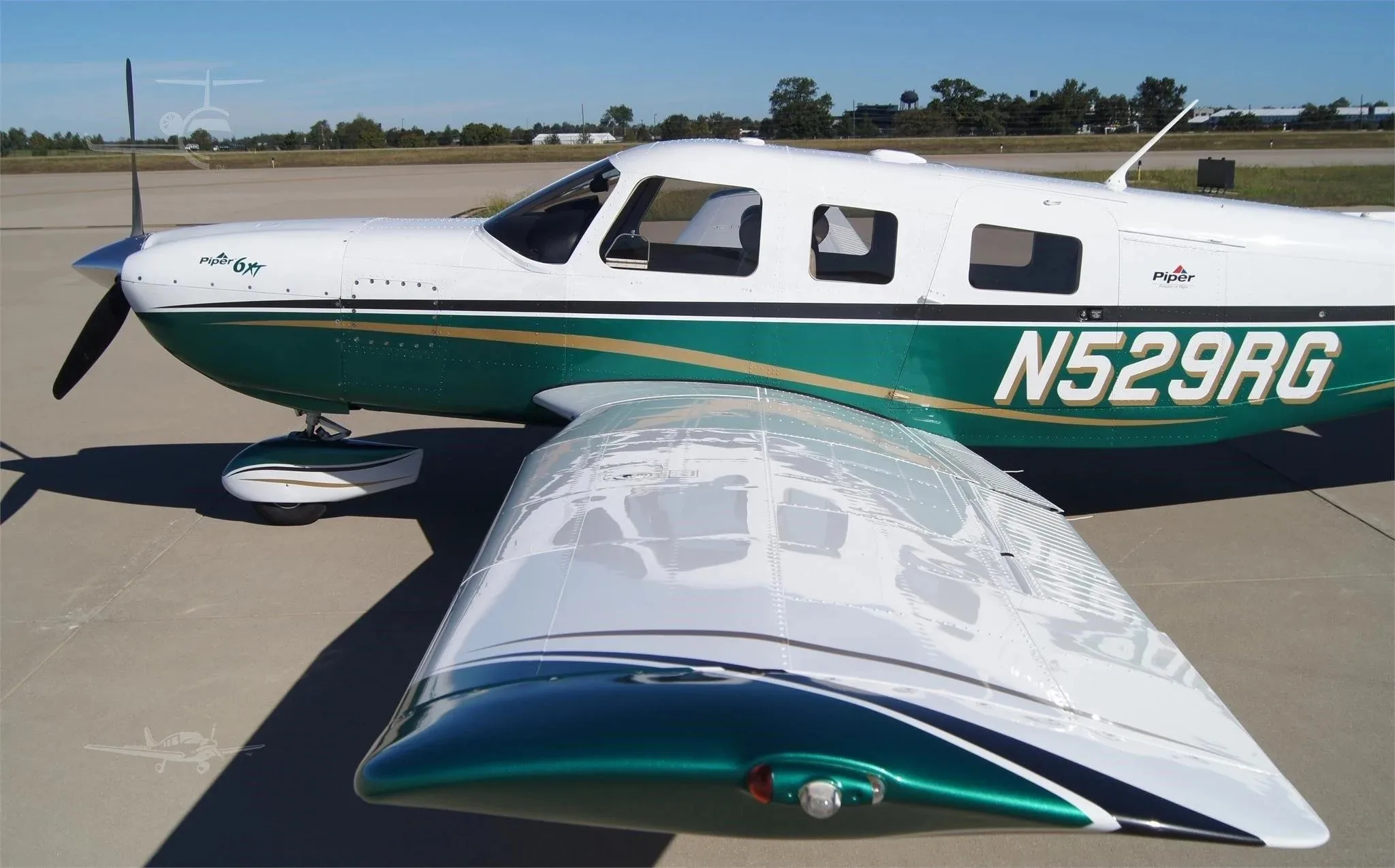 A close-up side view of the white and green Piper 6XT (N529RG) showing the propeller and wing on an airfield.