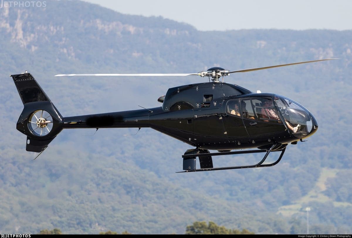 A black helicopter in flight with a mountainous background.