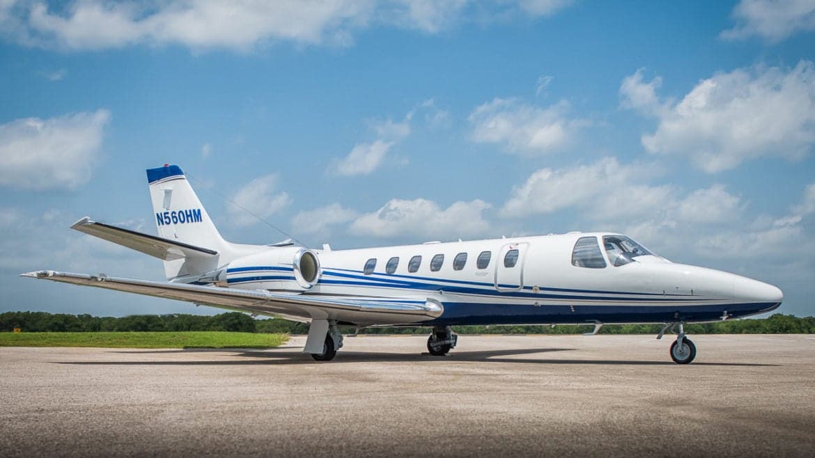 A Cessna Citation Encore sits on the tarmac with a blue and white paint scheme.