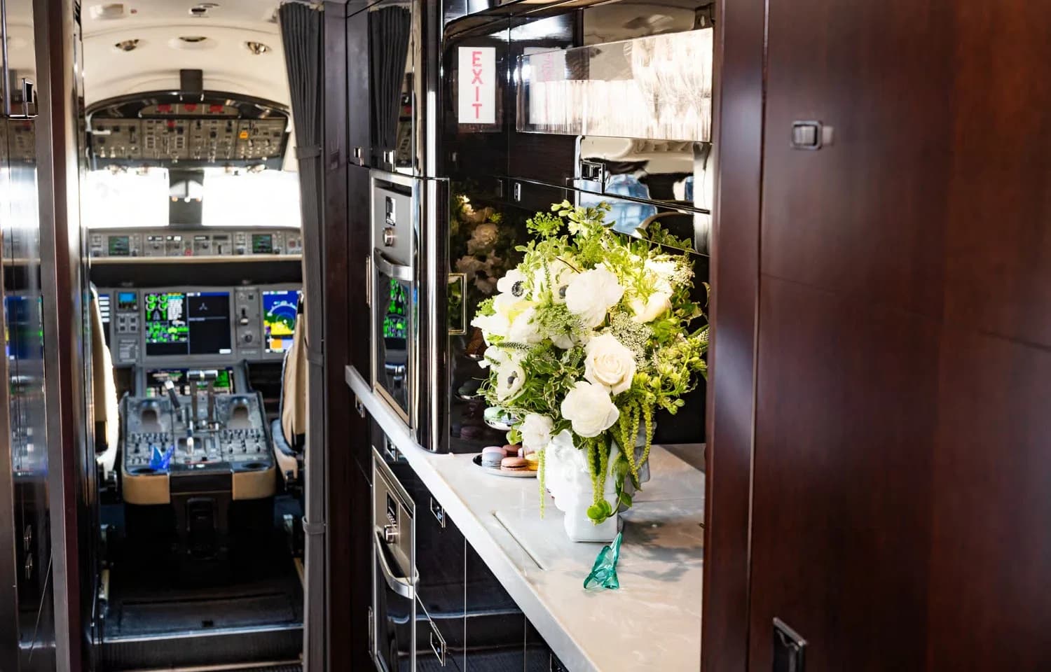 The private jet's galley area with a white floral arrangement on a counter, offering a glimpse into the cockpit.