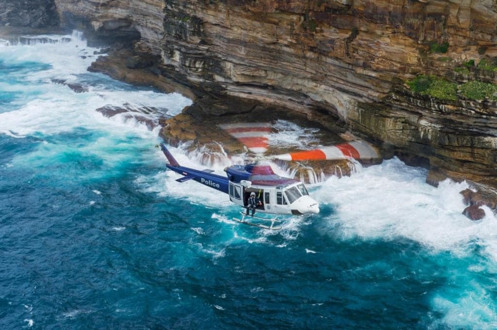 Police helicopter flying near rocky coastline with crashing waves.
