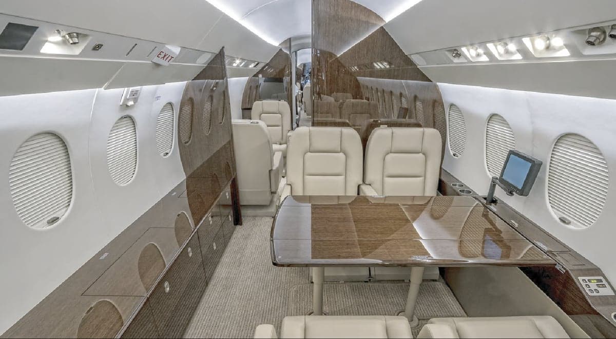 View of the interior cabin of a jet with leather seats and wood trim.