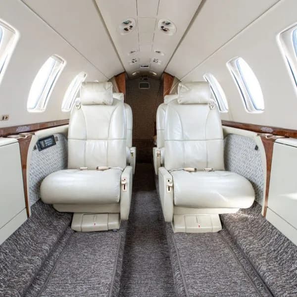 An interior view of an aircraft cabin with two rows of light beige leather seats facing each other.