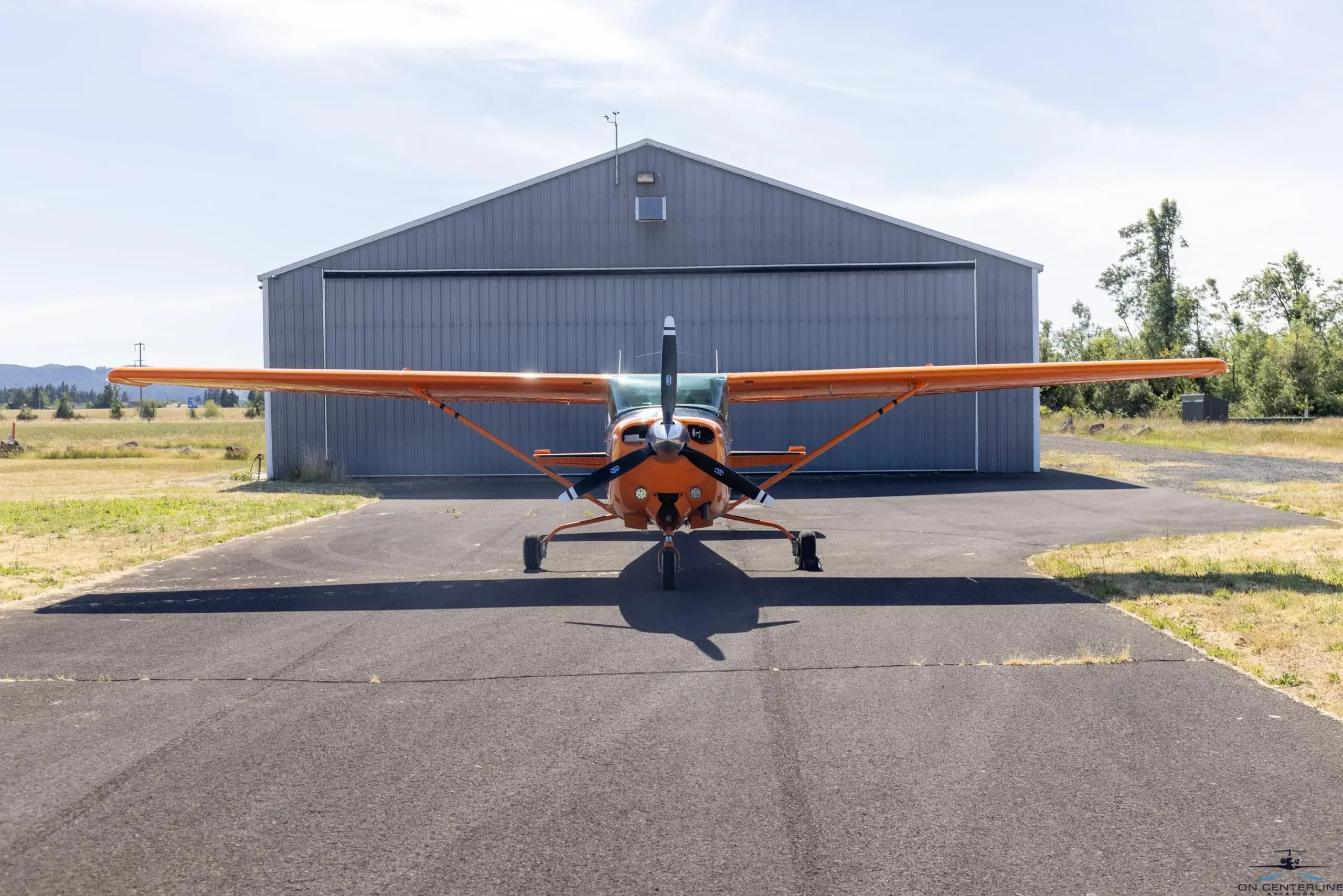 Front view of the orange and white Cessna 182 Skylane RG parked in front of a hangar.