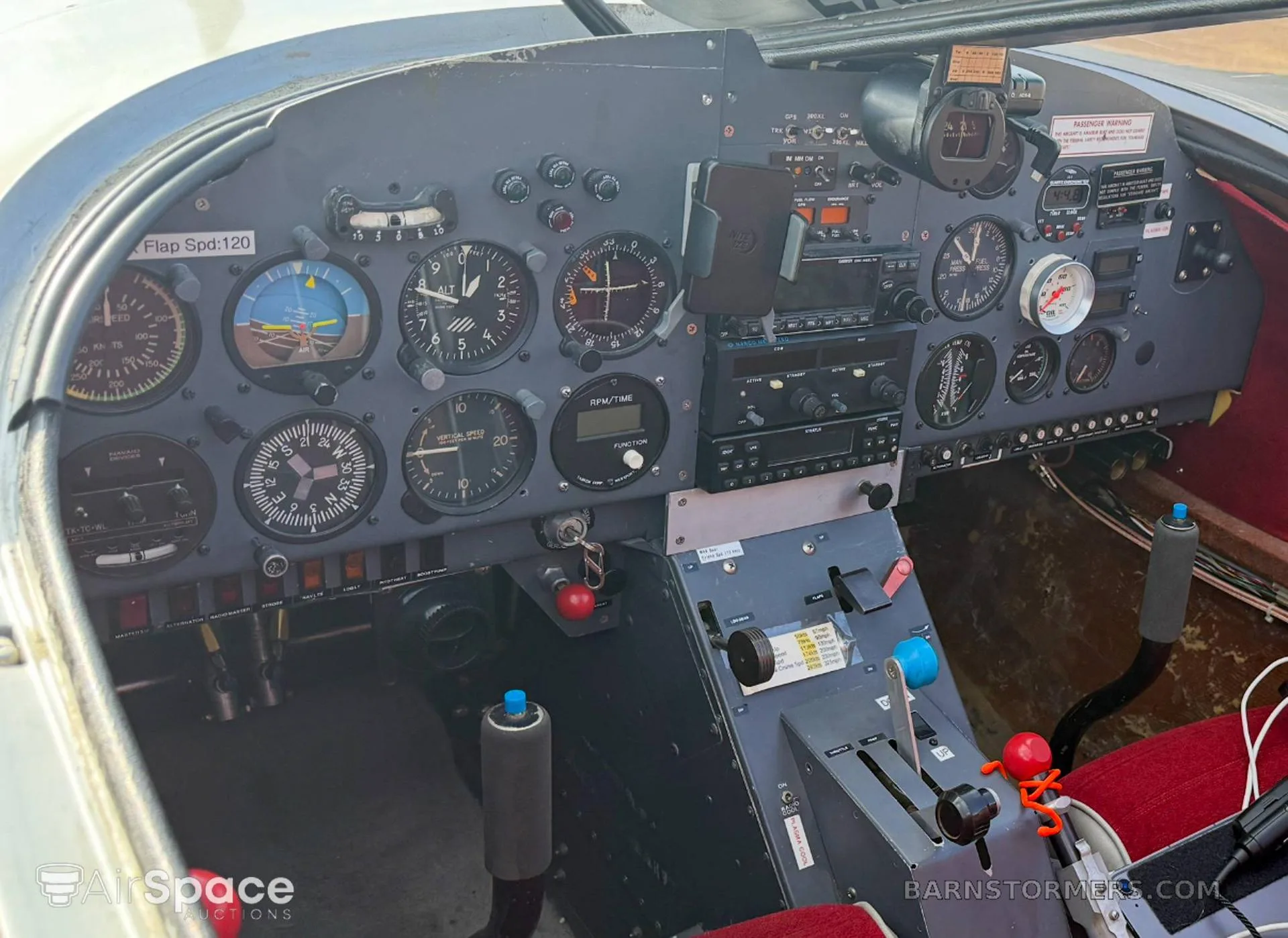 The cockpit of a small aircraft, showing the instrument panel with various gauges and controls, and red seats.