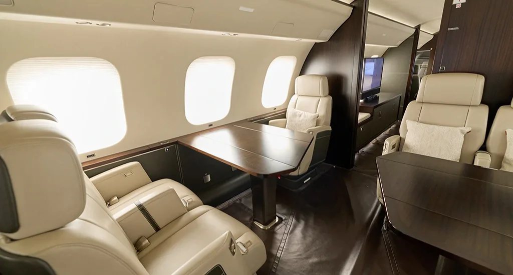 View of a private jet cabin with multiple cream leather seating areas and dark wooden tables.