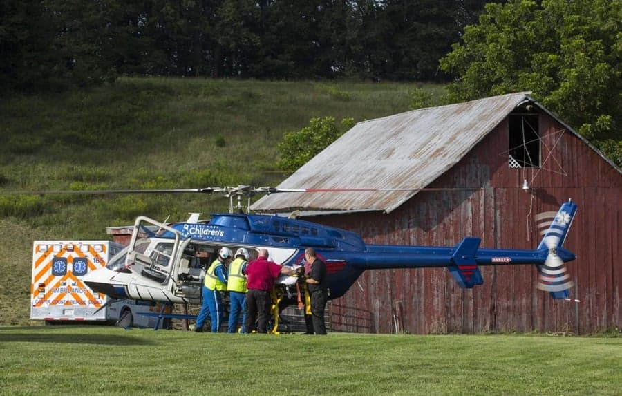 Air ambulance helicopter parked next to a barn with medical personnel attending to a patient.