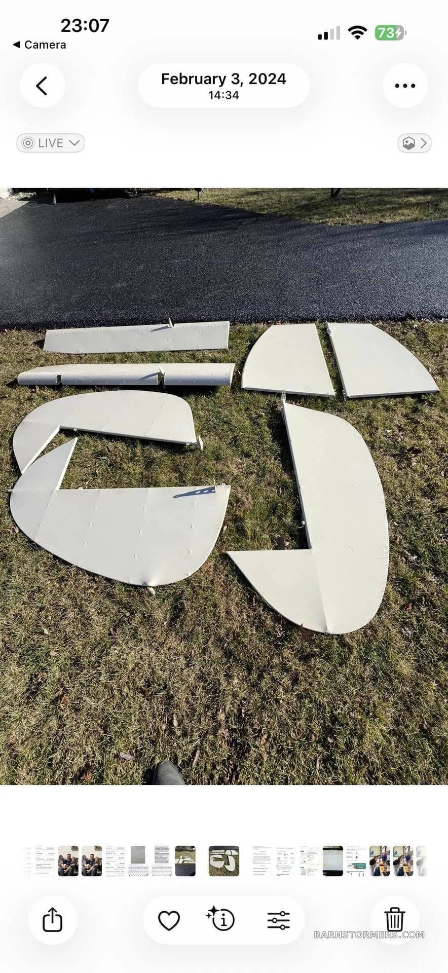 Various white aircraft components, including wings and tail sections, laid out on green grass.