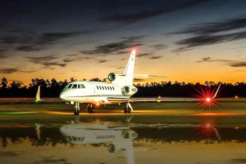 A Falcon jet sits on the tarmac at dusk.