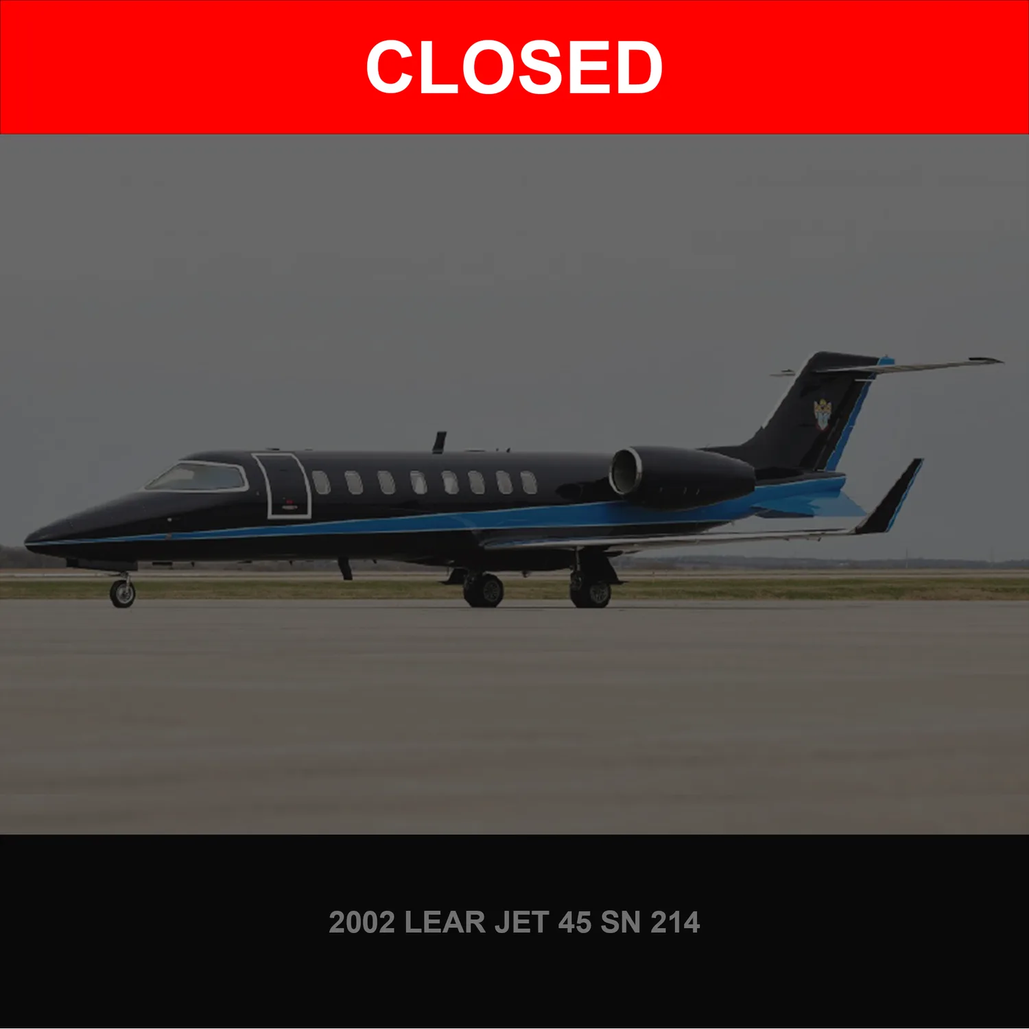 A black Learjet 45 with blue stripes on the fuselage and tail is parked on an asphalt runway under an overcast sky.