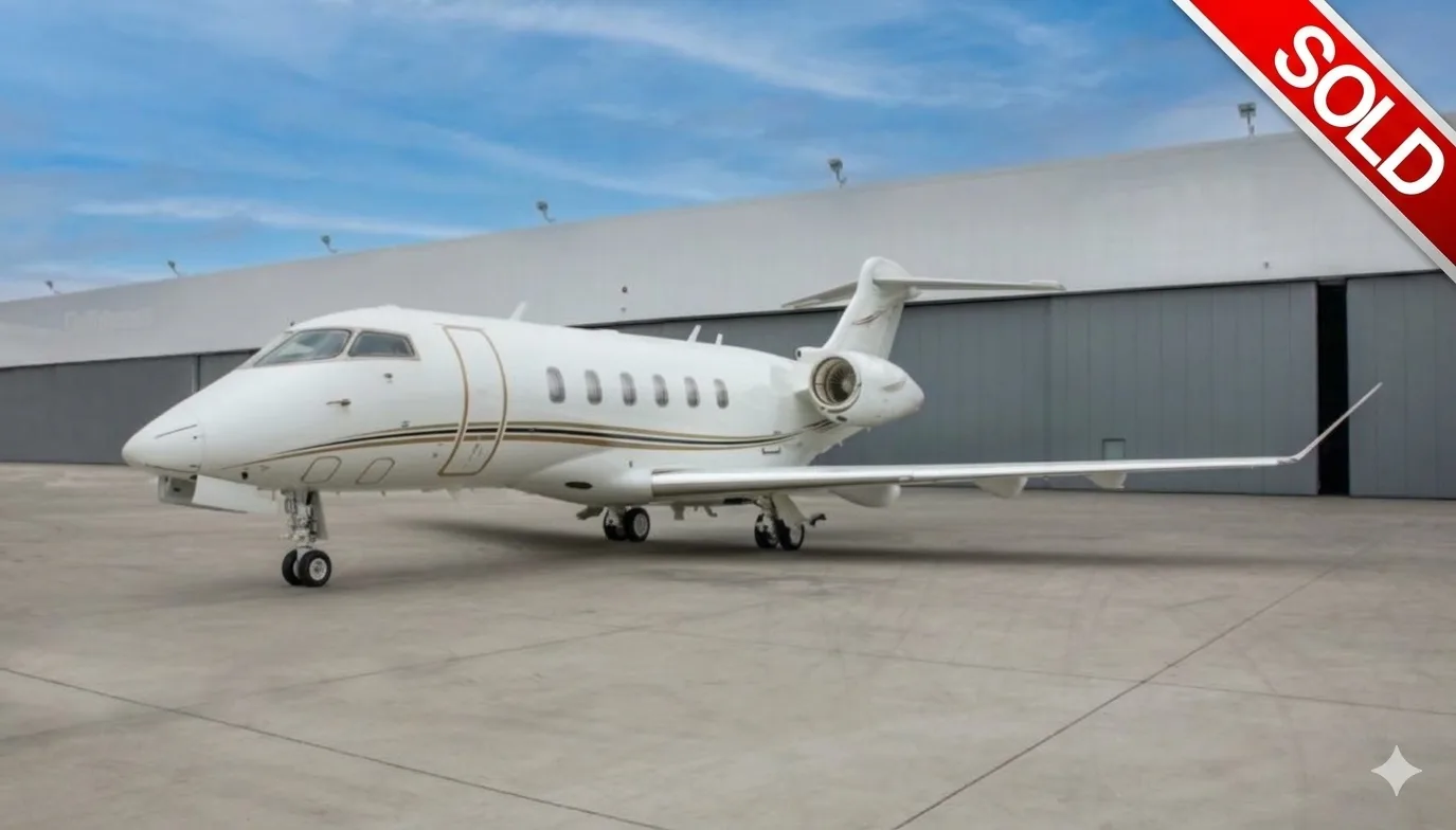 A white business jet with gold and brown stripes is parked on an tarmac in front of a hangar under a blue sky.