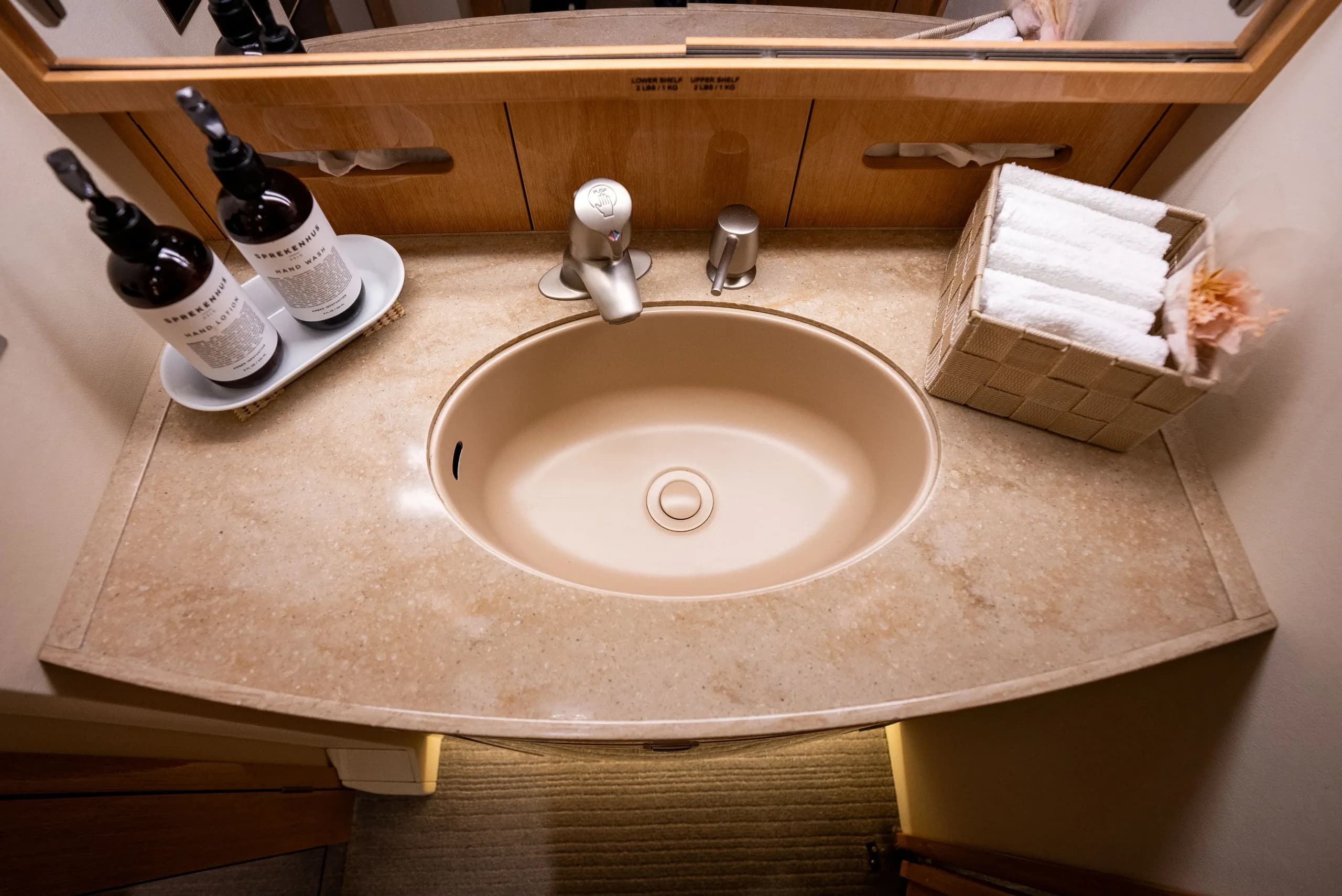 A private jet lavatory with a beige sink, marble countertop, hand soap, and neatly folded towels.