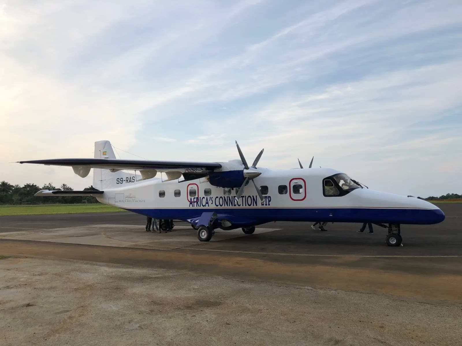 A white and blue twin-propeller aircraft with "Africa's Connection" livery parked on a tarmac with people standing nearby.