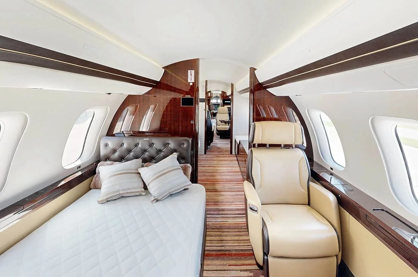 A private sleeping area in the Bombardier Global business jet cabin, with a quilted bed and a single beige armchair.