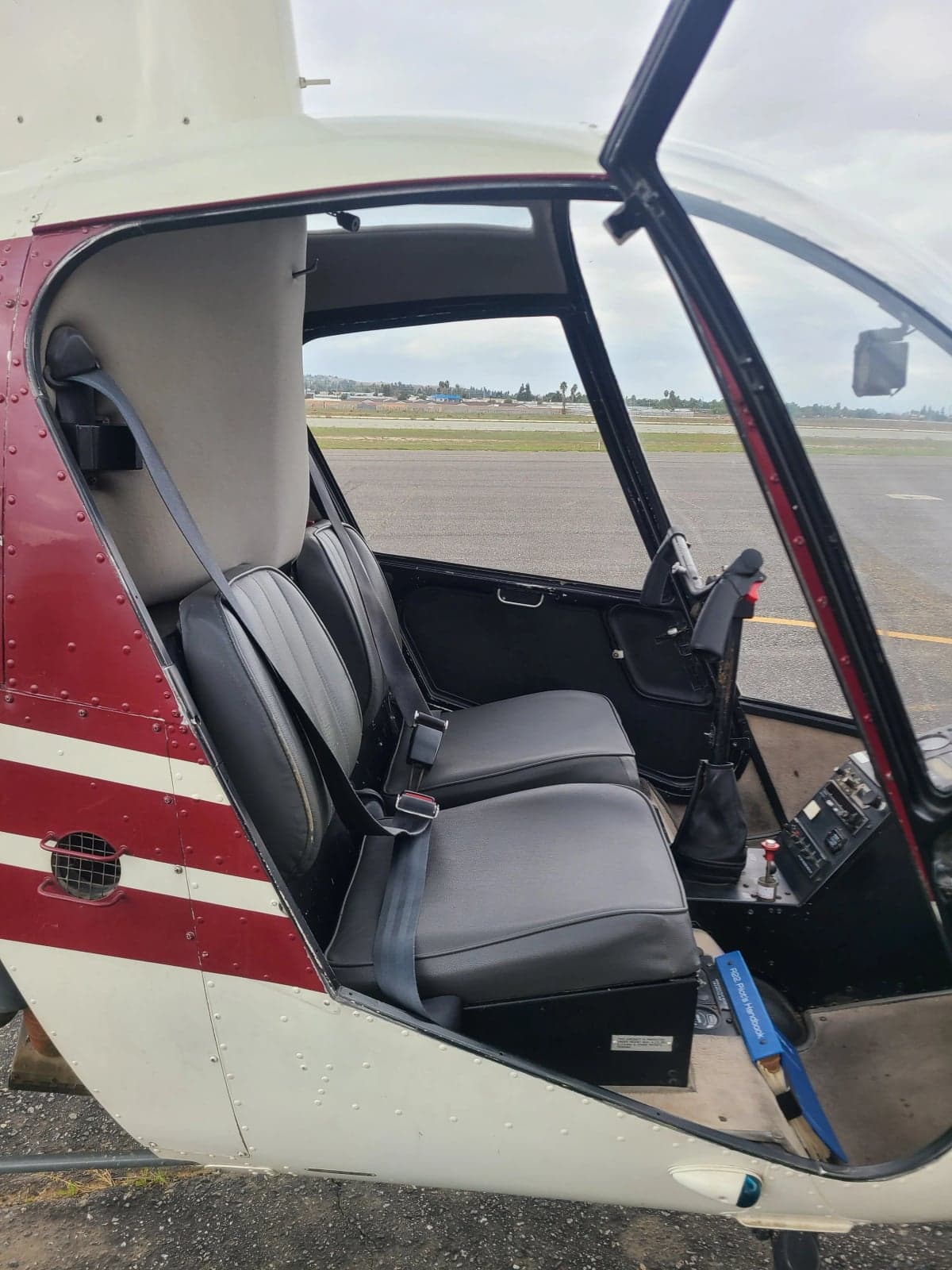 The two black seats and interior of a white and red Robinson R22 Beta helicopter, viewed from the side with the door open.