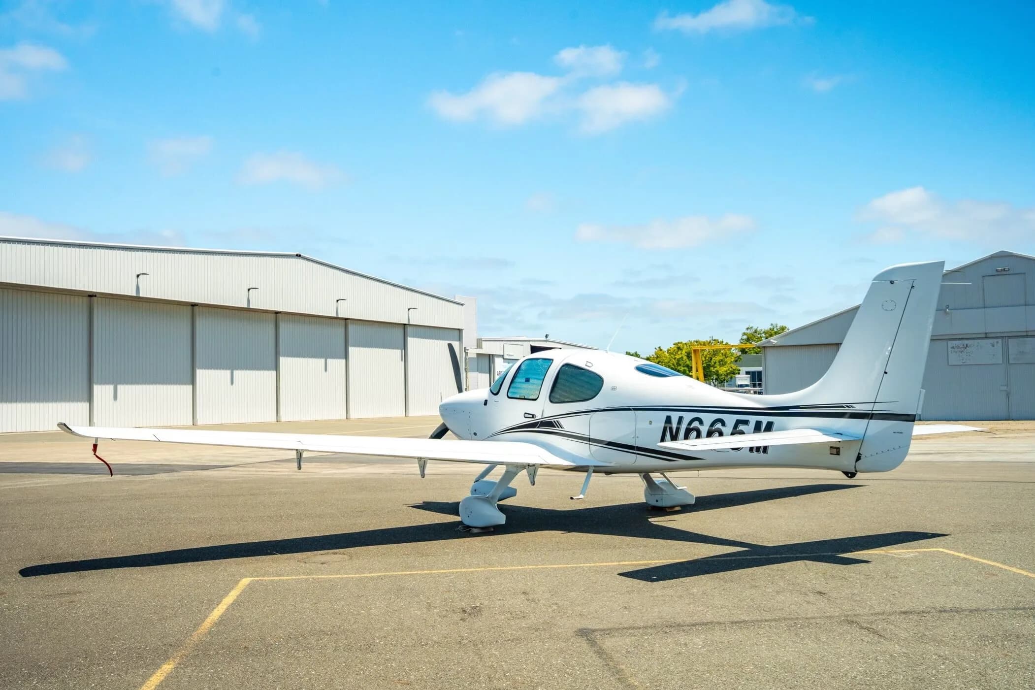 A white Cirrus SR22 aircraft with registration N665M parked on the tarmac, viewed from the rear side.