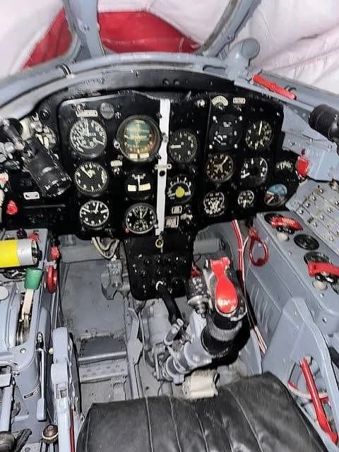 A wide view of a vintage jet aircraft cockpit, featuring the main instrument panel and various controls.