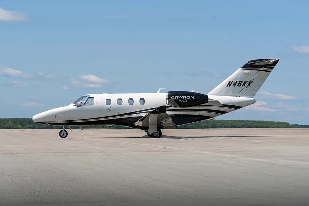 A white and black Citation M2 business jet with registration N46KK parked on an airfield under a blue sky.