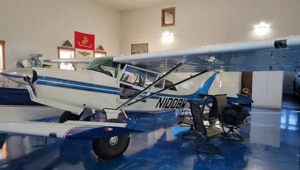 A white and blue Maule aircraft, N1008W, parked inside a hangar with a blue floor.