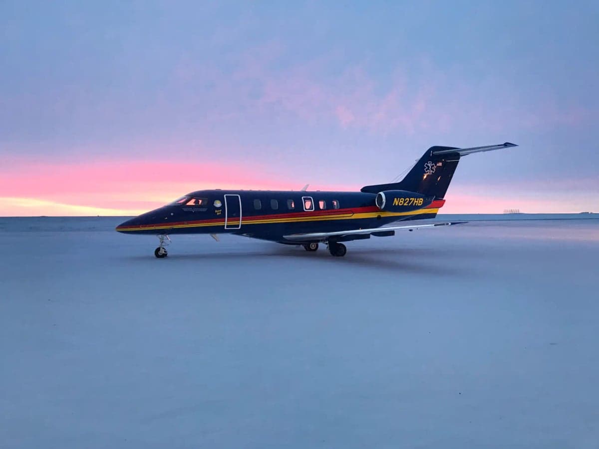 A Pilatus PC-24 aircraft parked on a snowy runway at sunset.