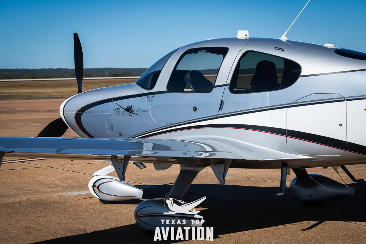 Close-up of the front fuselage and wing of a silver and white Cirrus SR22 aircraft.