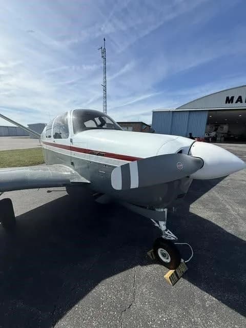 Front-side view of the N2194D Beechcraft Bonanza V-tail aircraft, parked on an airfield under a blue sky.