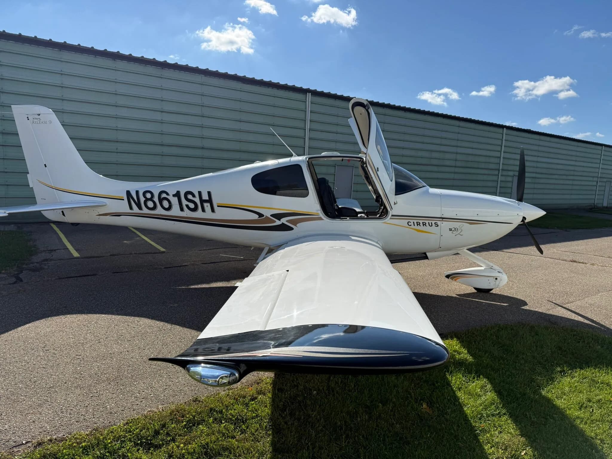 A front-side view of a white Cirrus SR20 aircraft, registration N861SH, with its right door open, parked on an asphalt ramp.