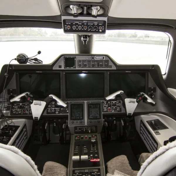 The modern cockpit of an Embraer Phenom 100 jet, featuring multiple digital displays and controls, with tail number N858EE visible.