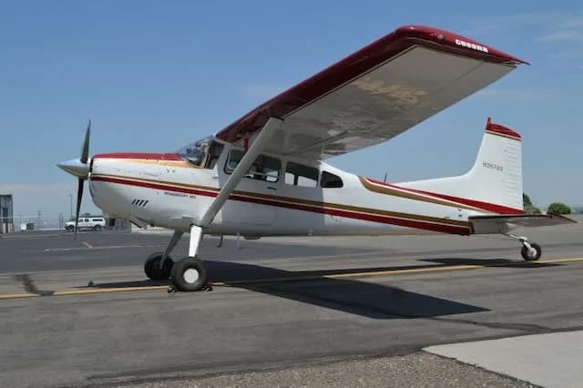 A white Cessna Stationair 6 with red and gold stripes is parked on an asphalt tarmac under a clear blue sky.