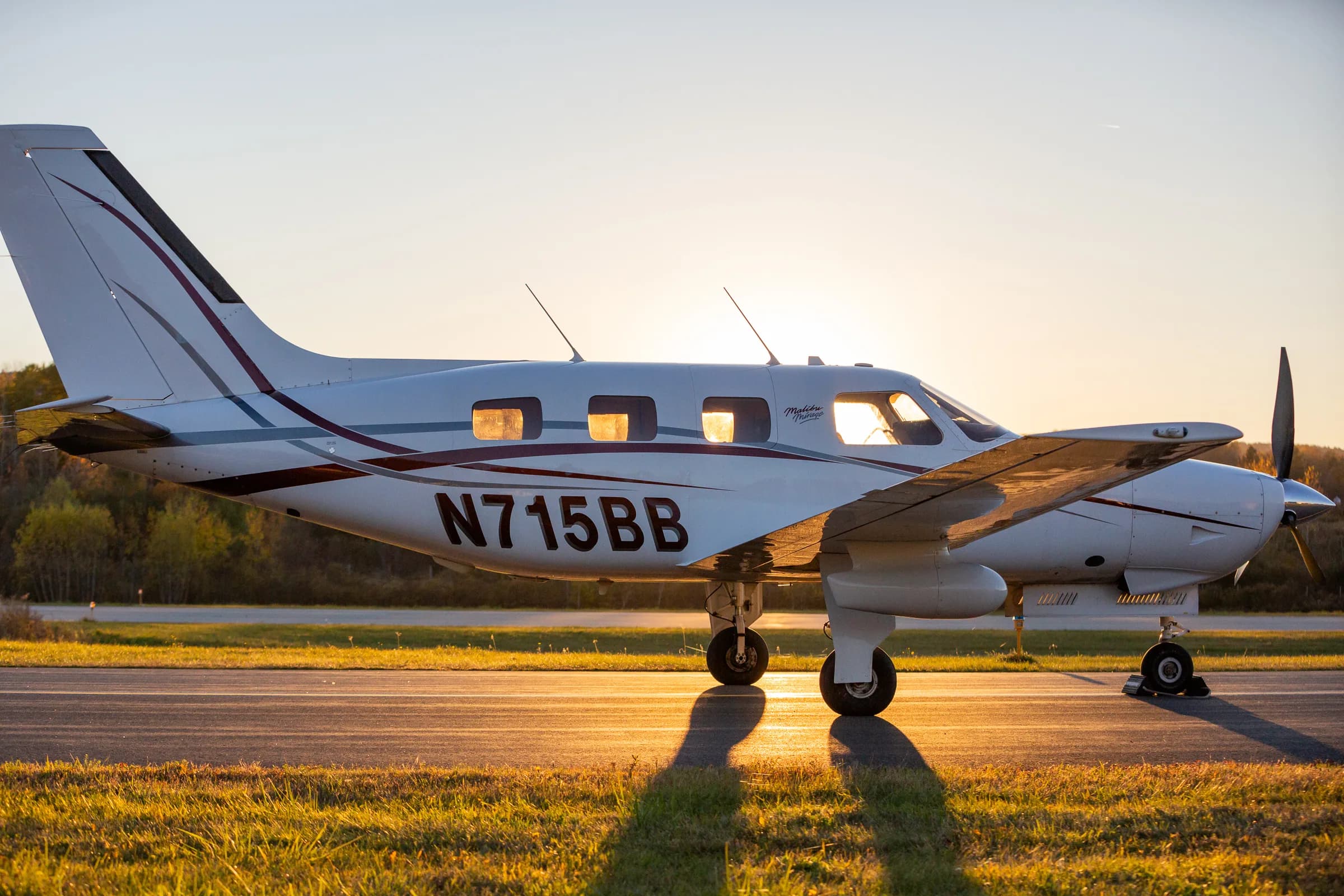 A side view of the Piper Malibu Mirage N715BB with its propeller at sunset on a runway.