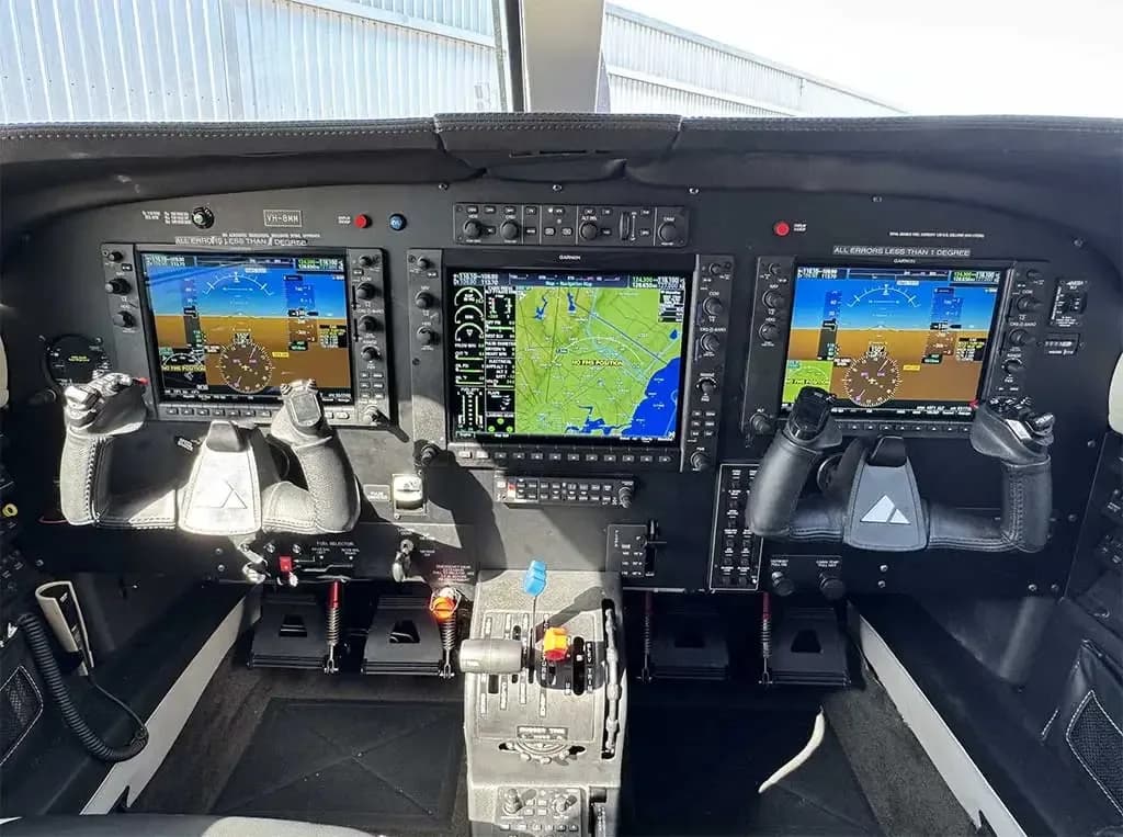 The cockpit features a modern glass panel with three large Garmin displays, two control yokes, and a central throttle quadrant.